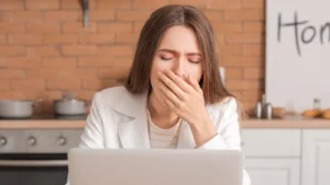 Mulher bocejando em frente ao laptop, sentindo cansaço constante e fadiga. Um dos 5 sinais de que a fadiga pode estar afetando sua saúde, abordado pela Infusion Cascavel.