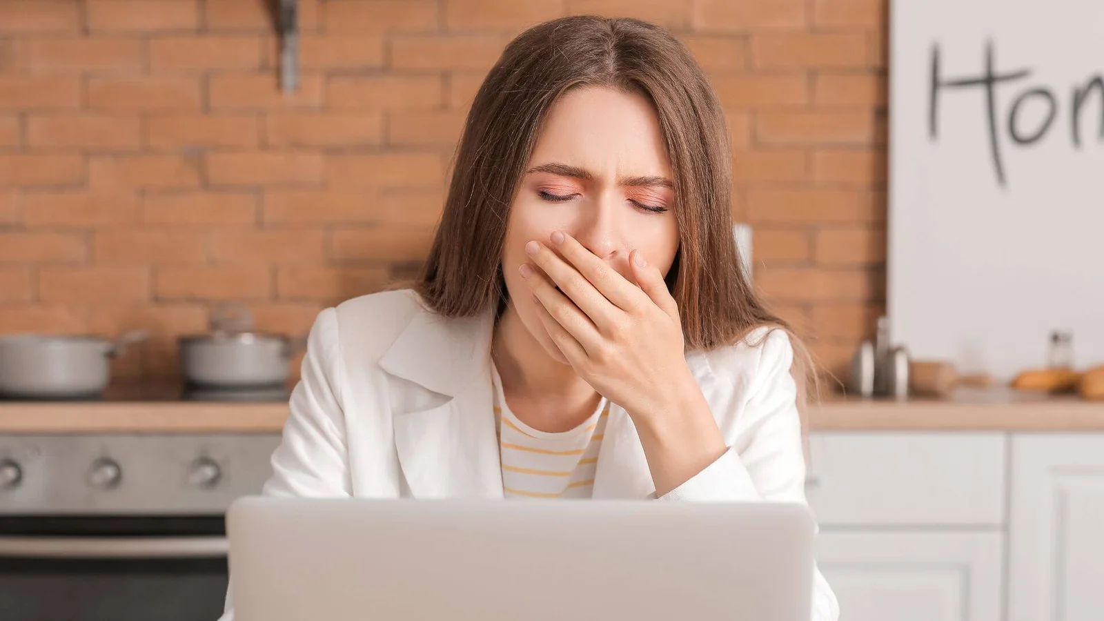 Mulher bocejando em frente ao laptop, sentindo cansaço constante e fadiga. Um dos 5 sinais de que a fadiga pode estar afetando sua saúde, abordado pela Infusion Cascavel.